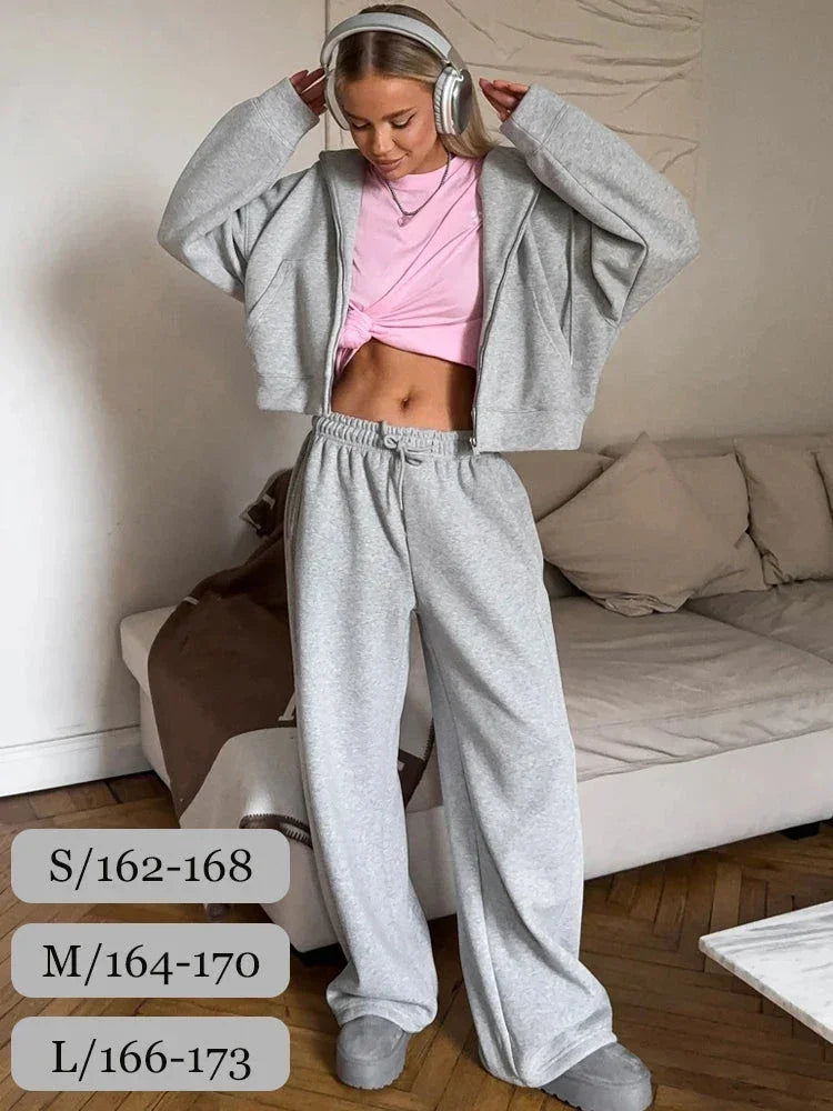 Woman in gray sweatpants and cropped hoodie with pink knotted top wearing headphones indoors