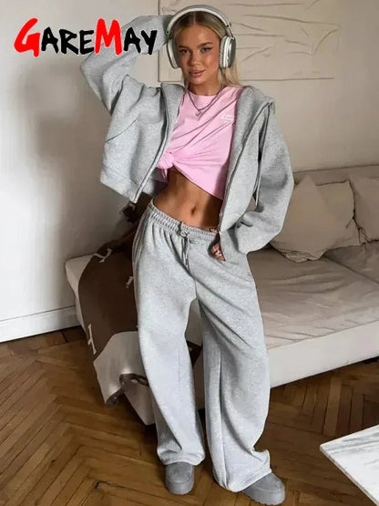 Woman in gray sweatpants, cropped hoodie, pink knotted top, wearing headphones, standing in living room