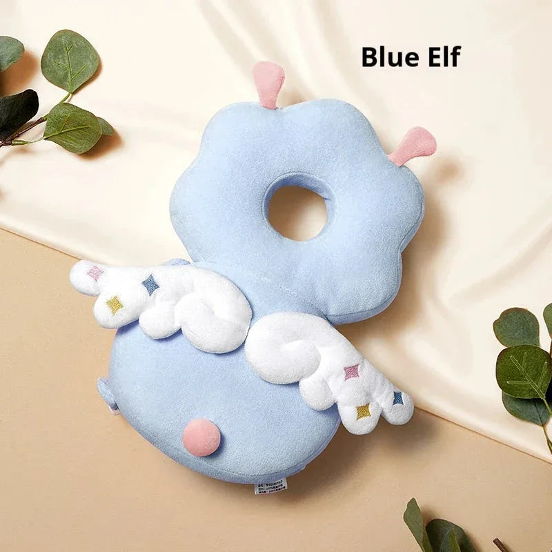 Blue elf baby head protection pillow with white wings and pink accents on a beige surface