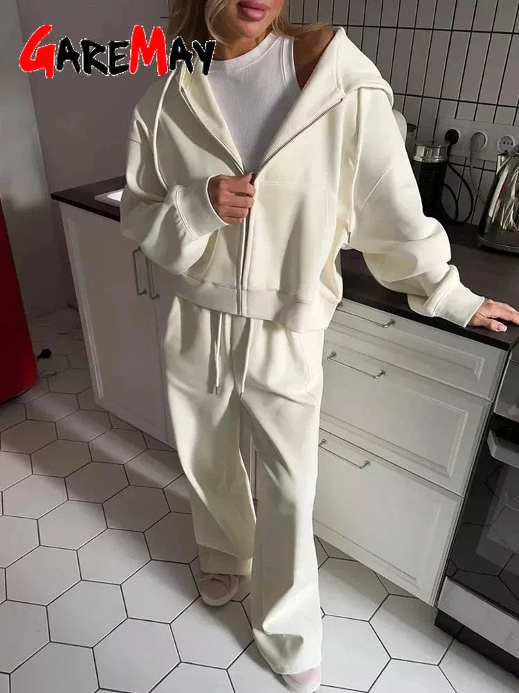 Woman in cream zip-up hoodie and matching wide-leg sweatpants standing in modern kitchen with hex tile floor