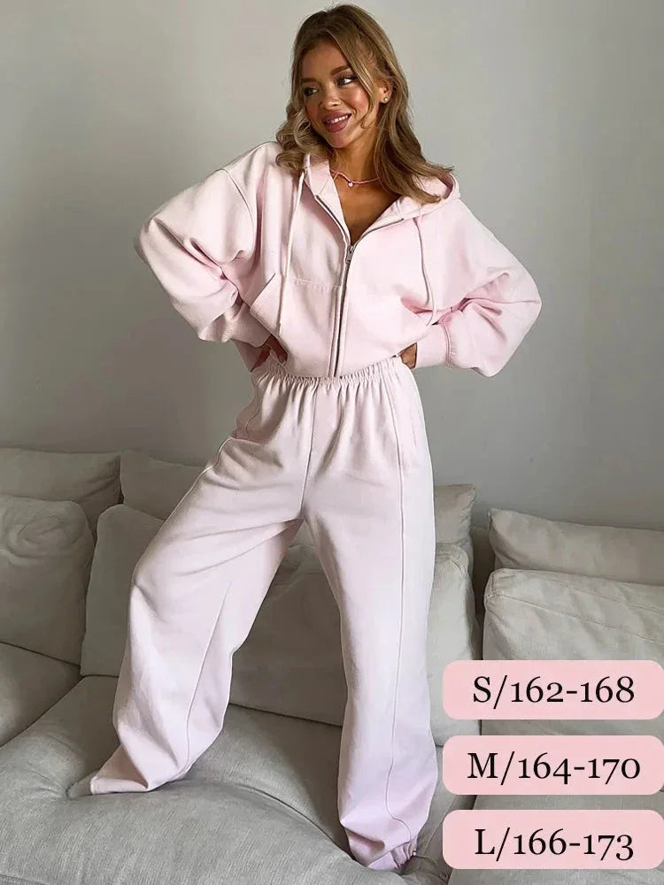Woman wearing light pink zip-up hoodie and matching sweatpants standing on couch in minimalist room