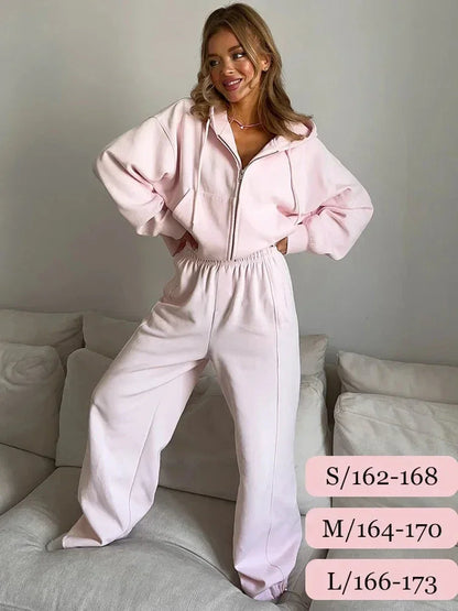 Woman wearing light pink zip-up hoodie and matching sweatpants standing on couch in minimalist room