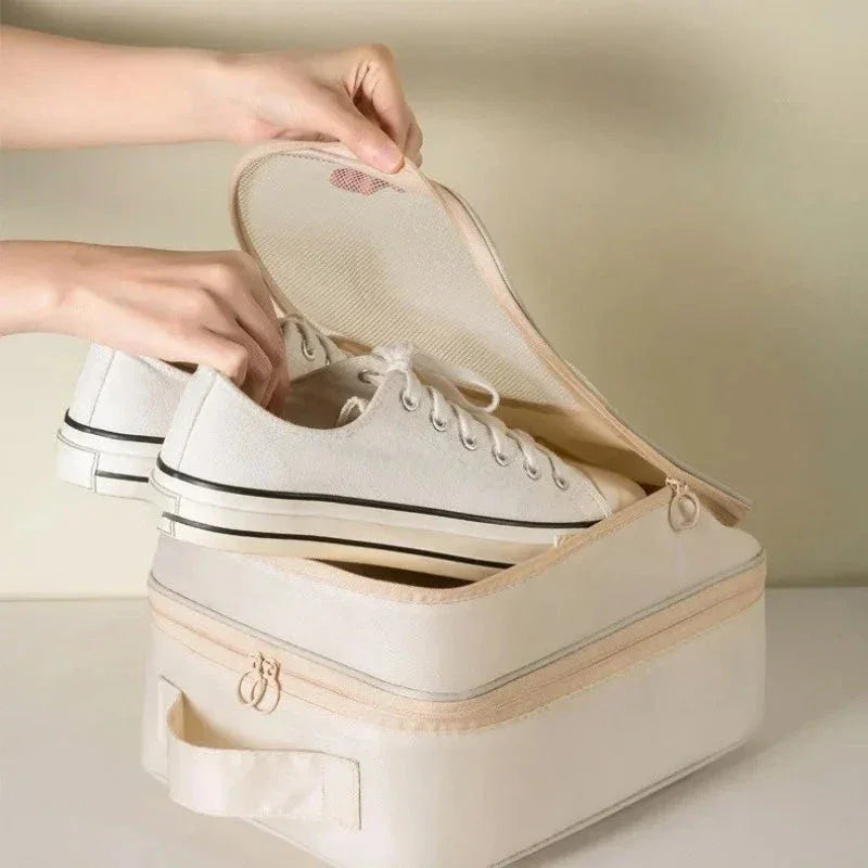Person placing white canvas sneakers inside beige travel shoe bag with zipper and handle