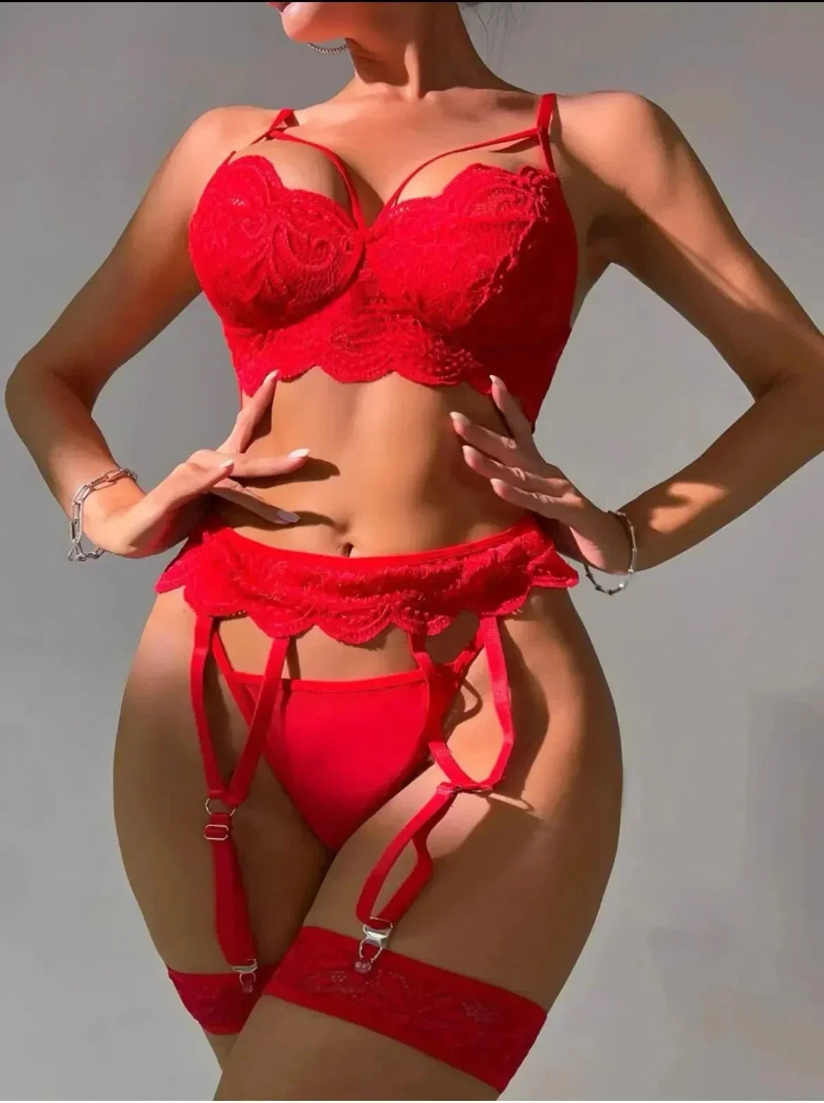 Woman wearing red lace lingerie set with garter belt and thigh-high stockings against gray background