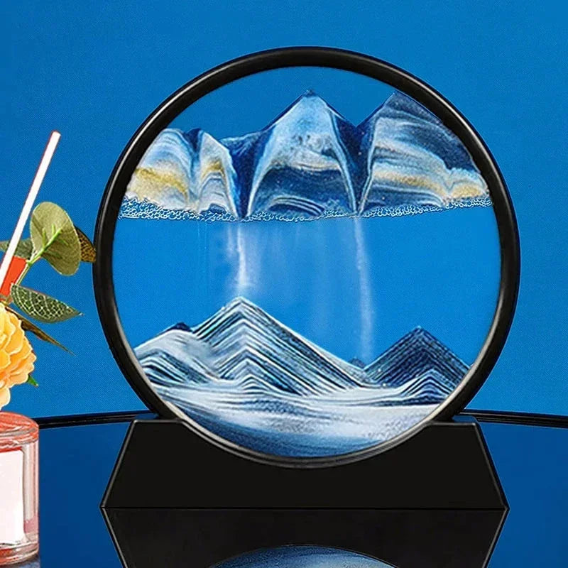 Round dynamic sand art with blue and white sand creating mountain landscapes on black stand against blue background