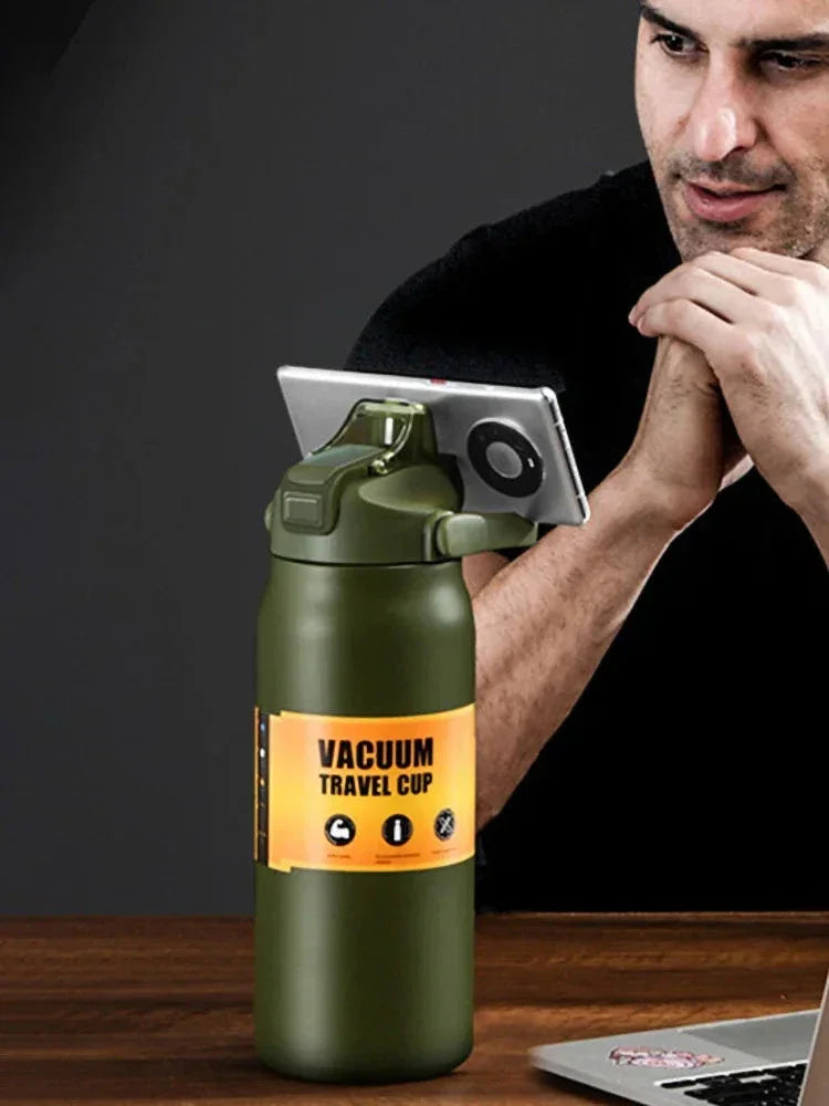 Green vacuum travel cup with smartphone holder standing on wooden table near man in black shirt