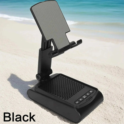 Black portable wireless speaker with phone holder on sandy beach by ocean