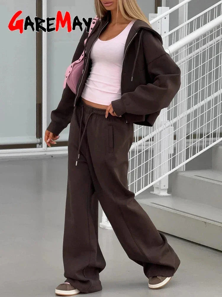 Woman wearing dark brown oversized hoodie and sweatpants with white tank top and pink shoulder bag indoors
