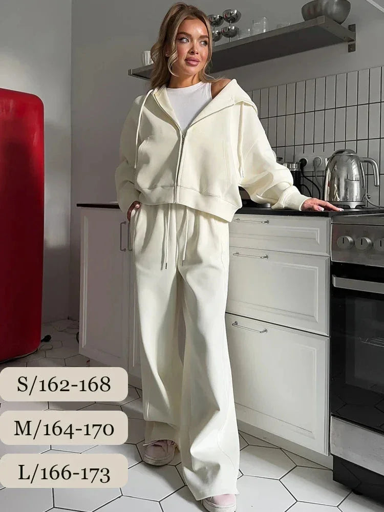 Woman in white oversized zip-up hoodie and wide-leg pants standing in modern kitchen with white cabinets and red fridge